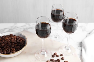 Glasses of coffee liqueur and beans on white table