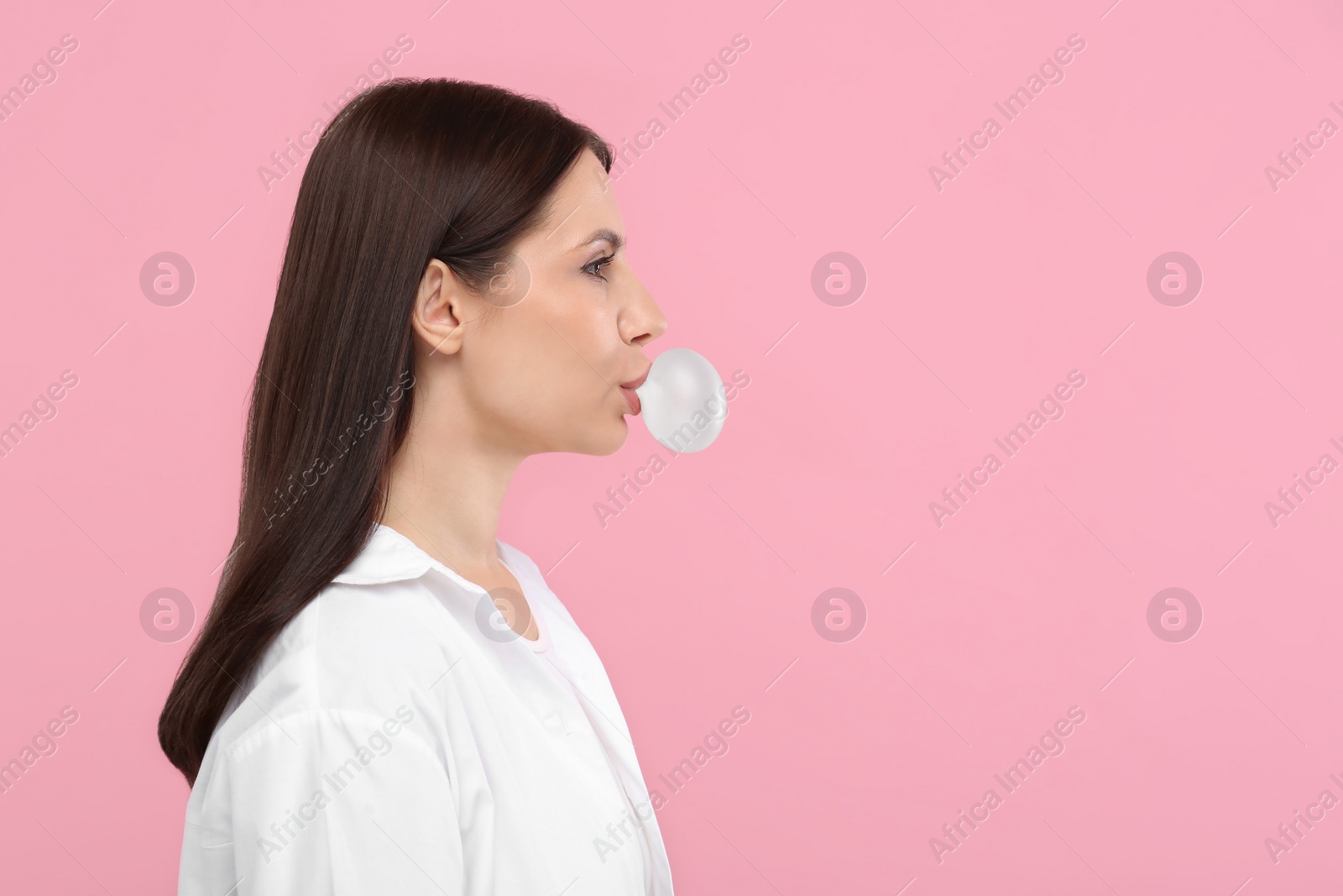 Photo of Beautiful woman blowing bubble gum on pink background, space for text