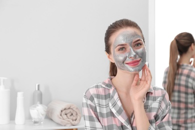 Photo of Young woman with cleansing mask on her face in bathroom, space for text. Skin care