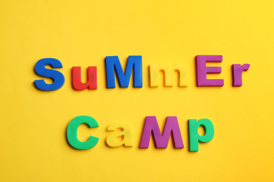 Photo of Phrase SUMMER CAMP made with magnet letters on yellow background, flat lay