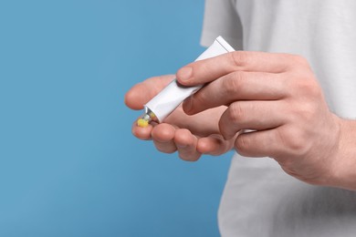 Photo of Man applying yellow ointment from tube onto his hand on light blue background, closeup. Space for text