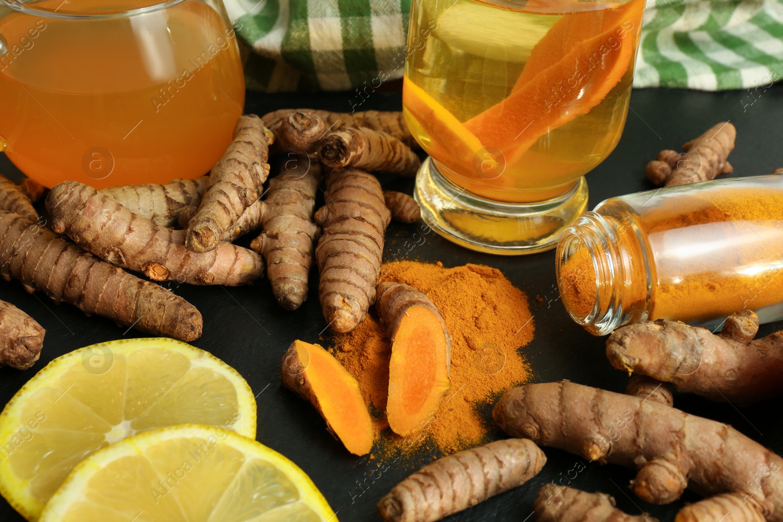 Photo of Turmeric roots, powder, sliced lemon and cup of tasty tea on black table