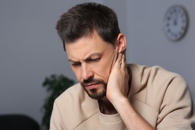 Man suffering from ear pain on in room