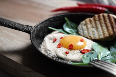 Delicious fried egg with spinach and chilli served on wooden table, closeup
