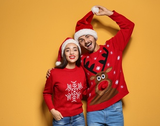 Photo of Young couple in Christmas sweaters and hats on color background