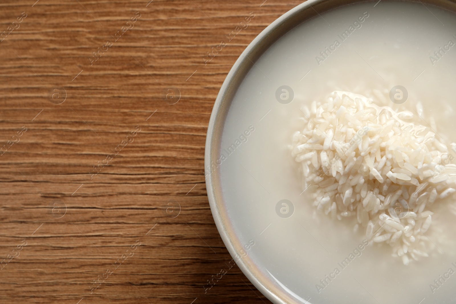 Photo of Rice soaked in water on wooden table, top view. Space for text