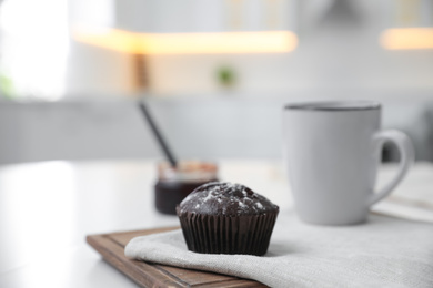 Delicious chocolate muffin on white table in kitchen. Space for text