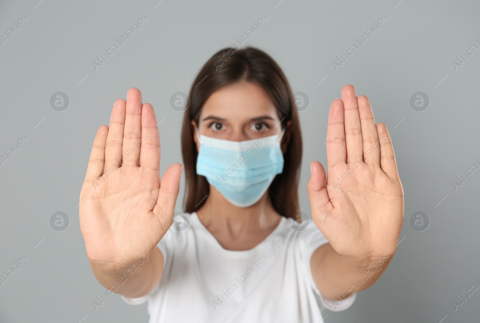 Photo of Woman in protective mask showing stop gesture on grey background. Prevent spreading of coronavirus