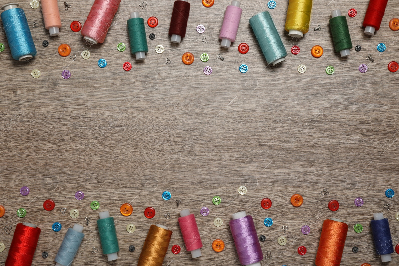 Photo of Frame of colorful buttons and threads on wooden background, flat lay. Space for text