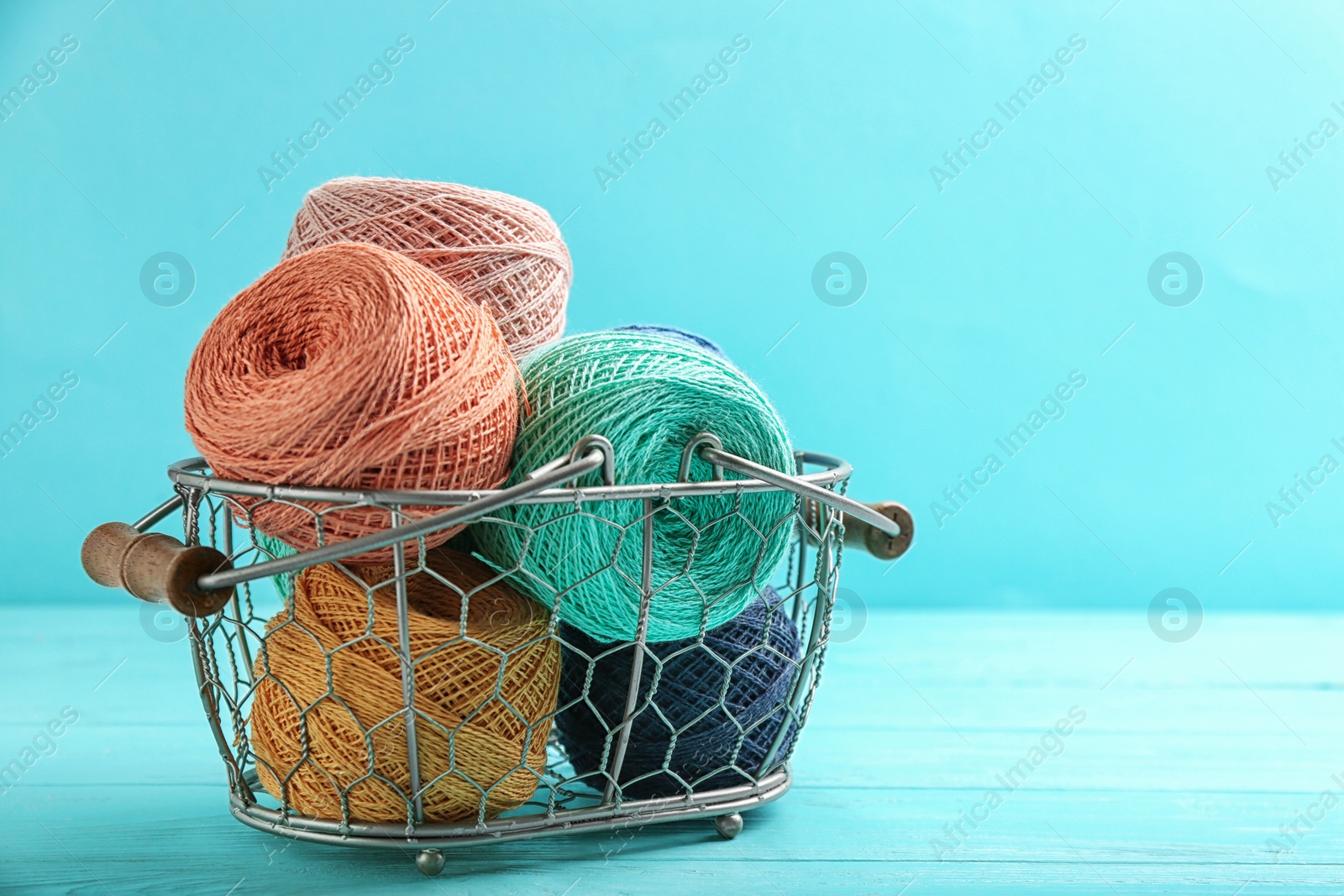 Photo of Clews of threads in basket on table against color background, space for text