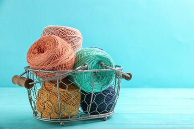 Photo of Clews of threads in basket on table against color background, space for text