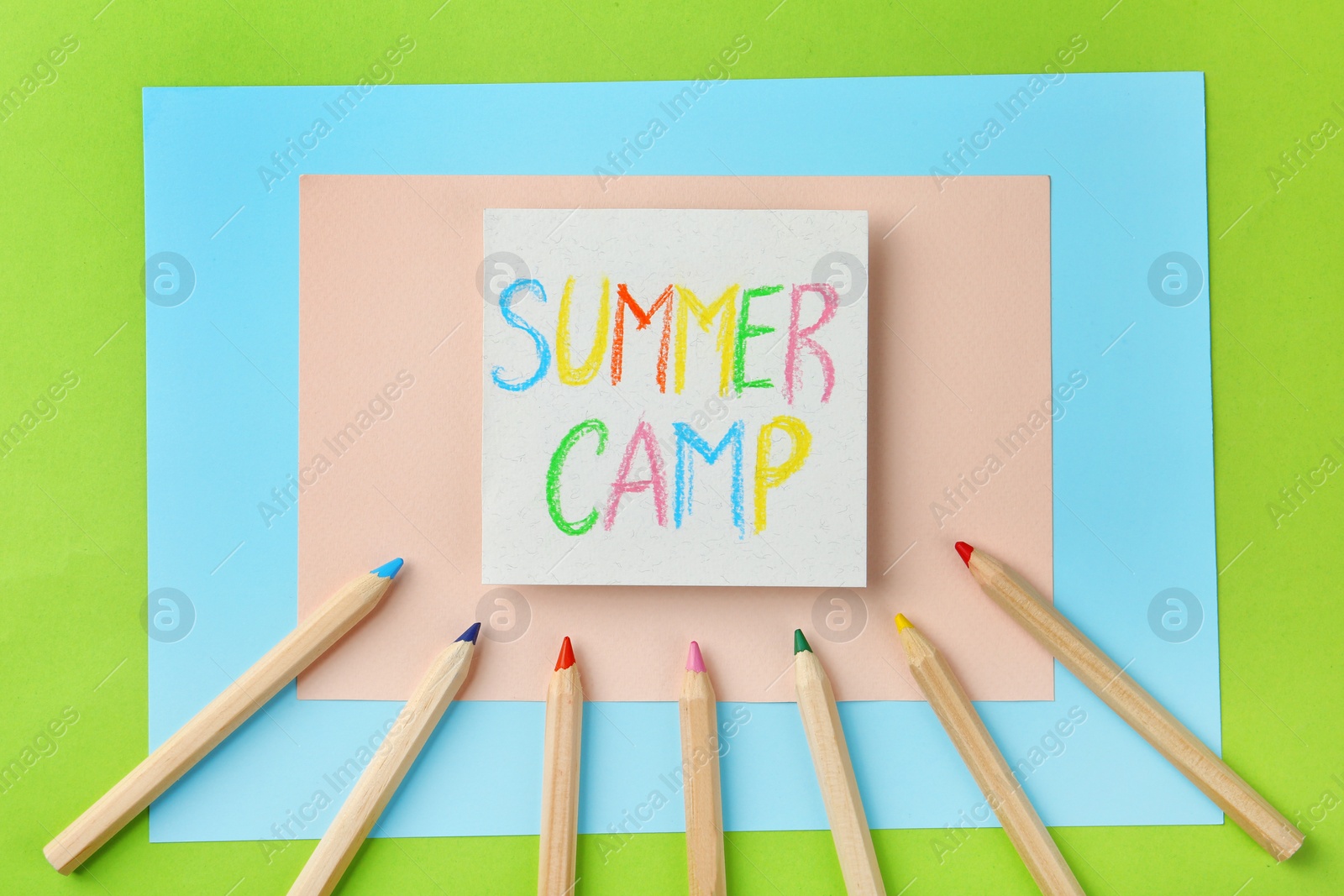 Photo of Paper with written text SUMMER CAMP and different pencils on color background, flat lay