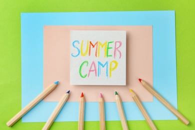 Photo of Paper with written text SUMMER CAMP and different pencils on color background, flat lay