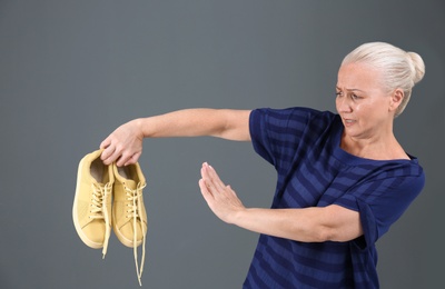 Woman feeling bad smell from shoes on color background. Air freshener