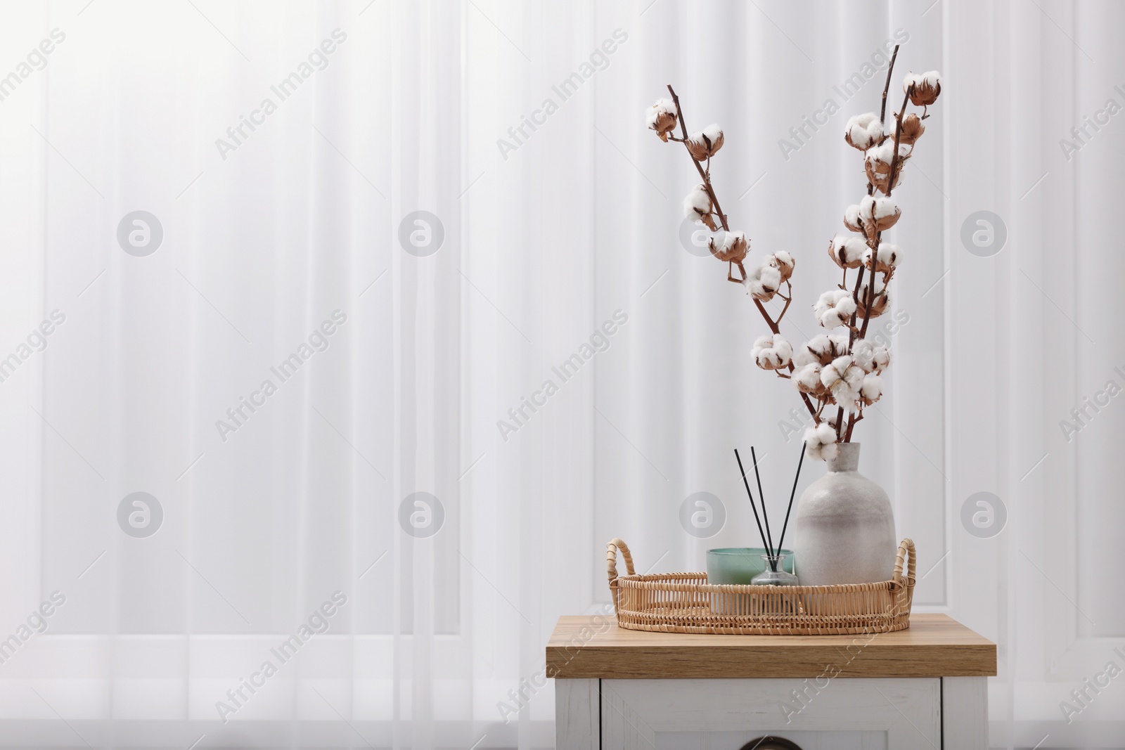 Photo of Candle, reed diffuser and vase with cotton branches on wooden commode indoors. Space for text