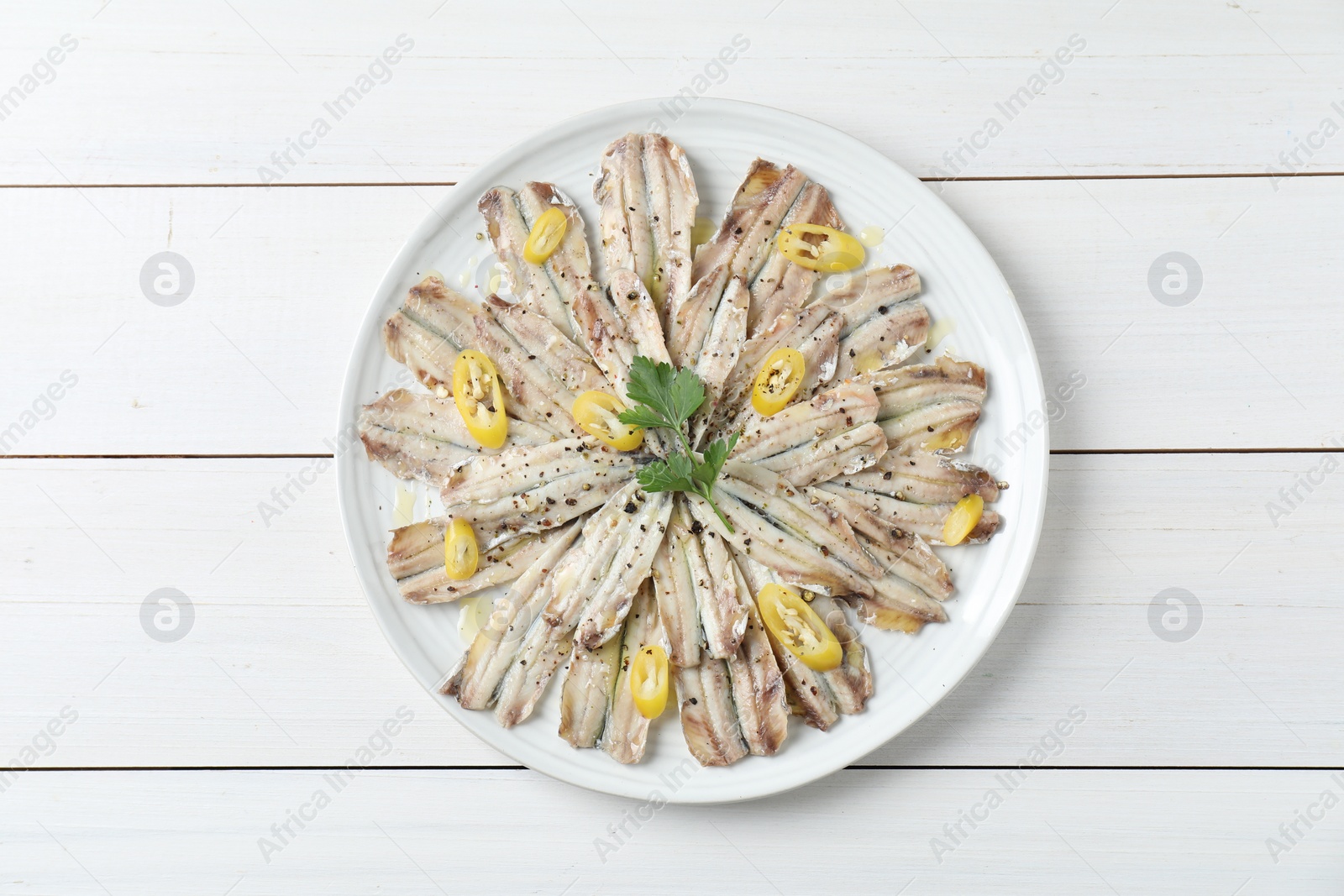 Photo of Tasty pickled anchovies with spices on white wooden table, top view