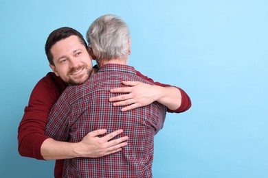 Happy son and his dad hugging on light blue background, space for text