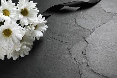 Photo of White chrysanthemum flowers and ribbon on black table, closeup with space for text. Funeral symbols