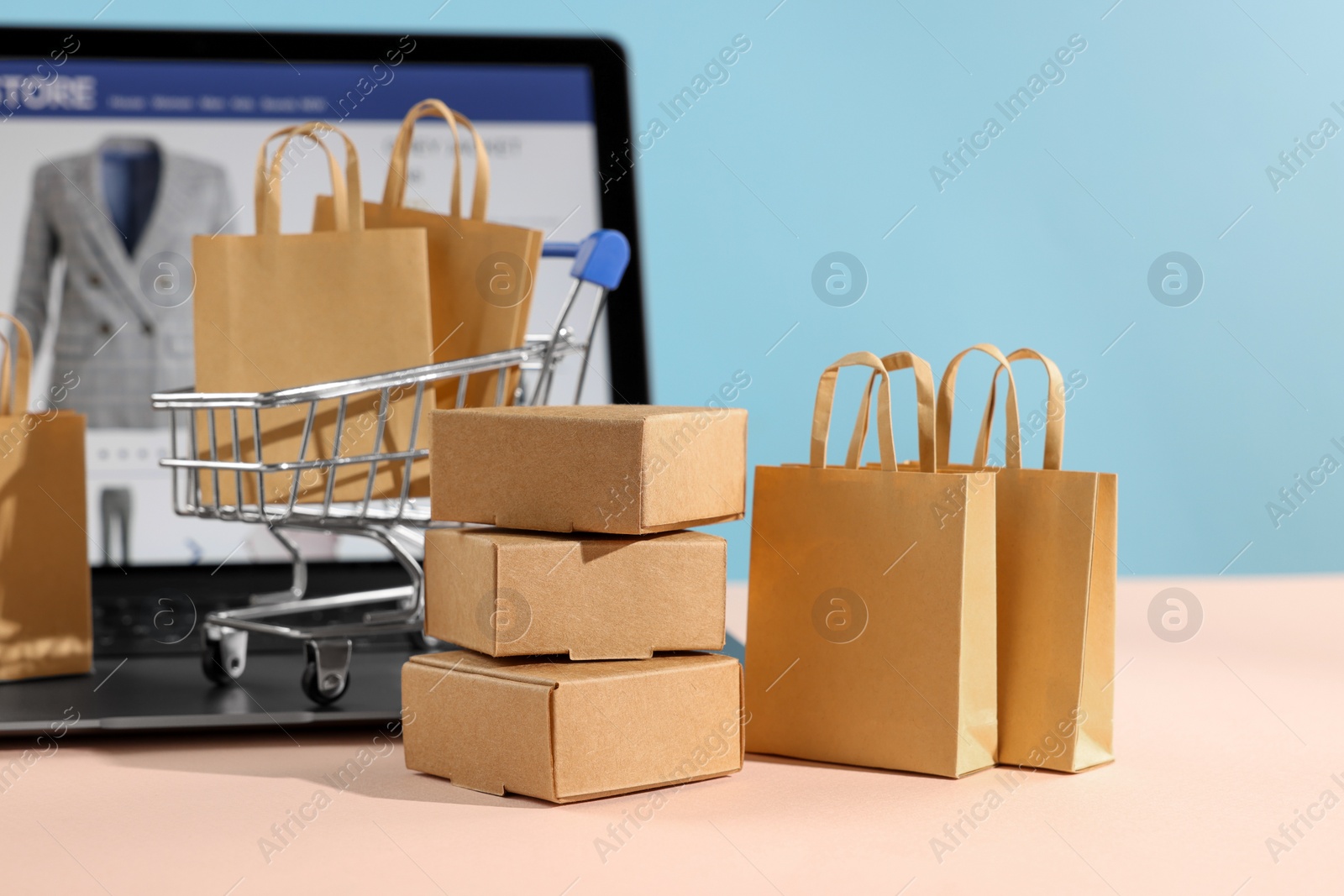 Photo of Online store. Purchases, mini shopping cart and laptop on beige table