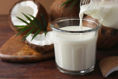 Photo of Pouring delicious coconut milk into glass on wooden table
