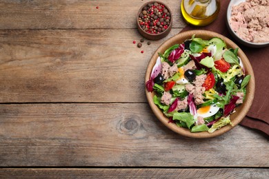 Photo of Bowl of delicious salad with canned tuna and vegetables on wooden table, flat lay. Space for text