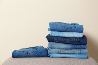 Stack of different jeans on ottoman against light background