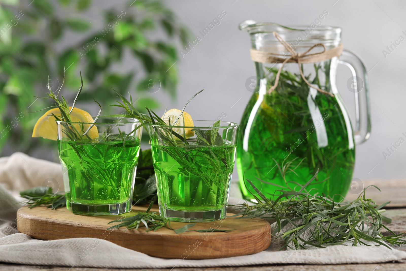 Photo of Glasses and jug of refreshing tarragon drink with lemon slices on table