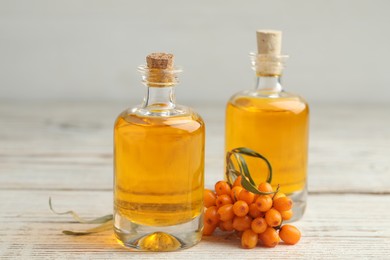 Photo of Natural sea buckthorn oil and fresh berries on white wooden table