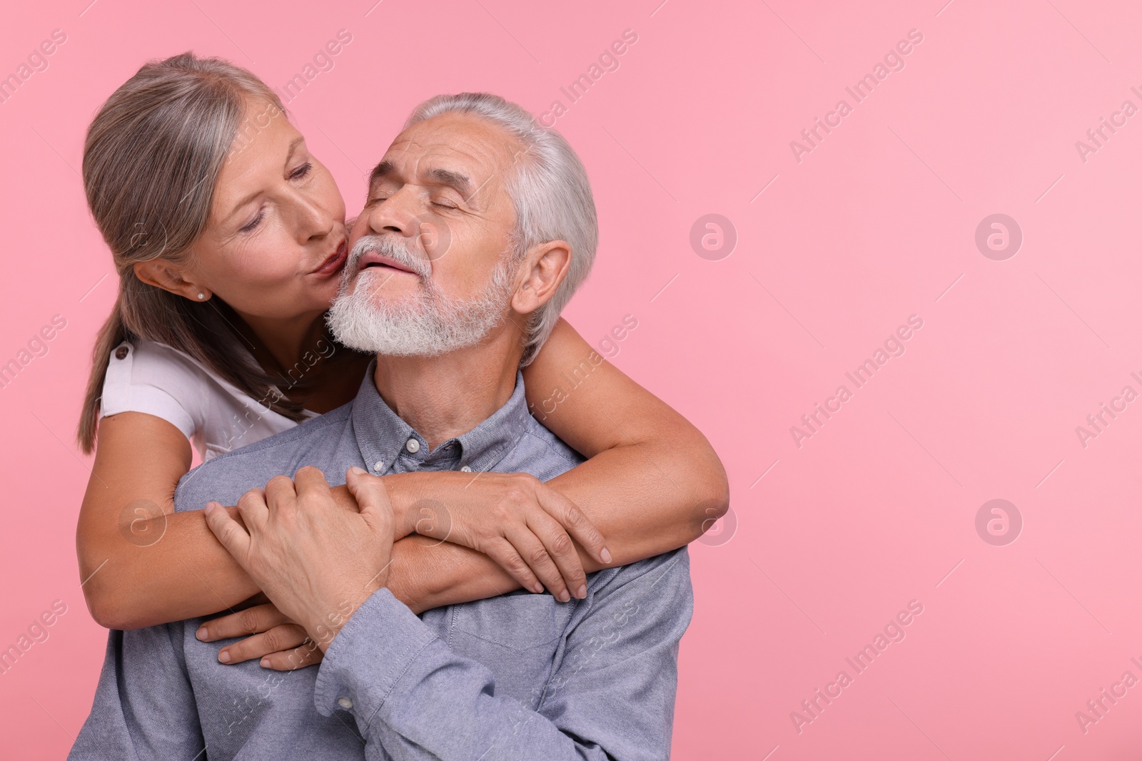 Photo of Senior woman kissing her beloved man on pink background, space for text