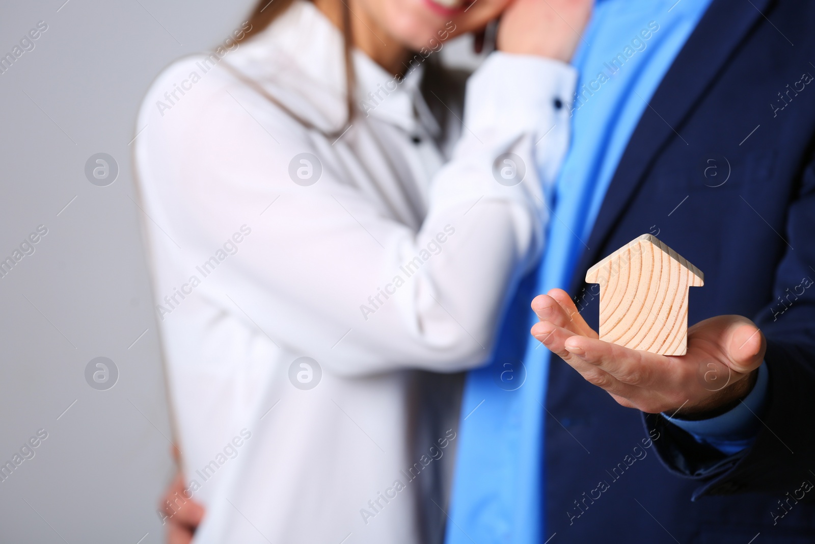 Photo of Young couple holding house figure on grey background, closeup. Home insurance