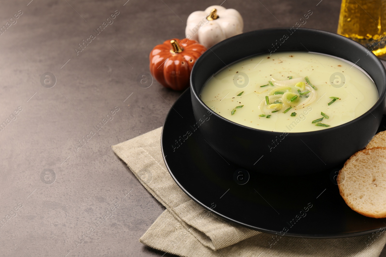 Photo of Bowl of tasty leek soup and bread on grey table, closeup. Space for text