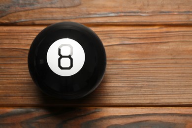 Photo of Magic eight ball on wooden table, top view. Space for text