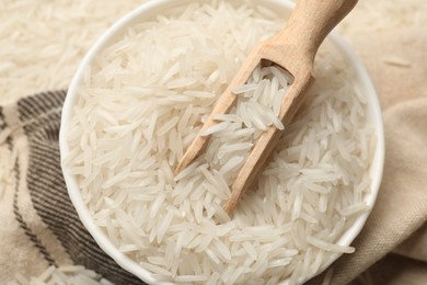 Photo of Raw basmati rice in bowl and scoop on cloth, top view