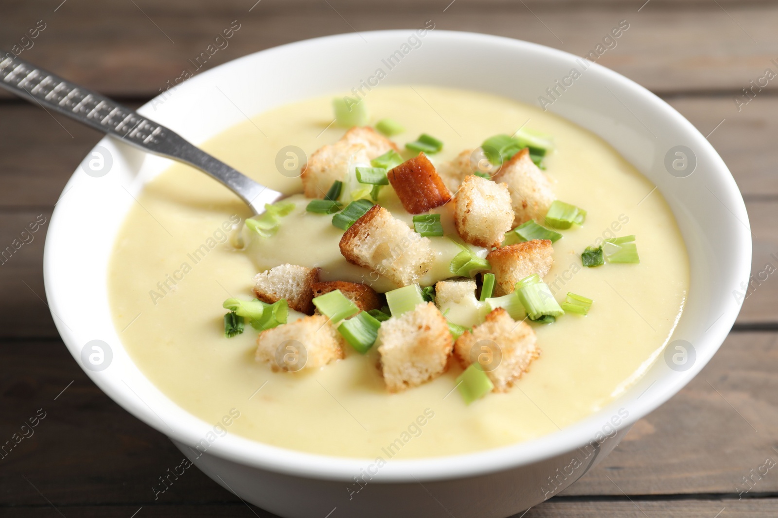 Photo of Tasty potato soup with croutons and spoon in bowl on wooden table, closeup