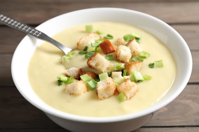 Photo of Tasty potato soup with croutons and spoon in bowl on wooden table, closeup