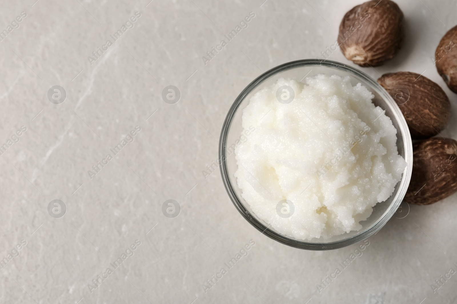 Photo of Shea butter in bowl and nuts on table, top view. Space for text