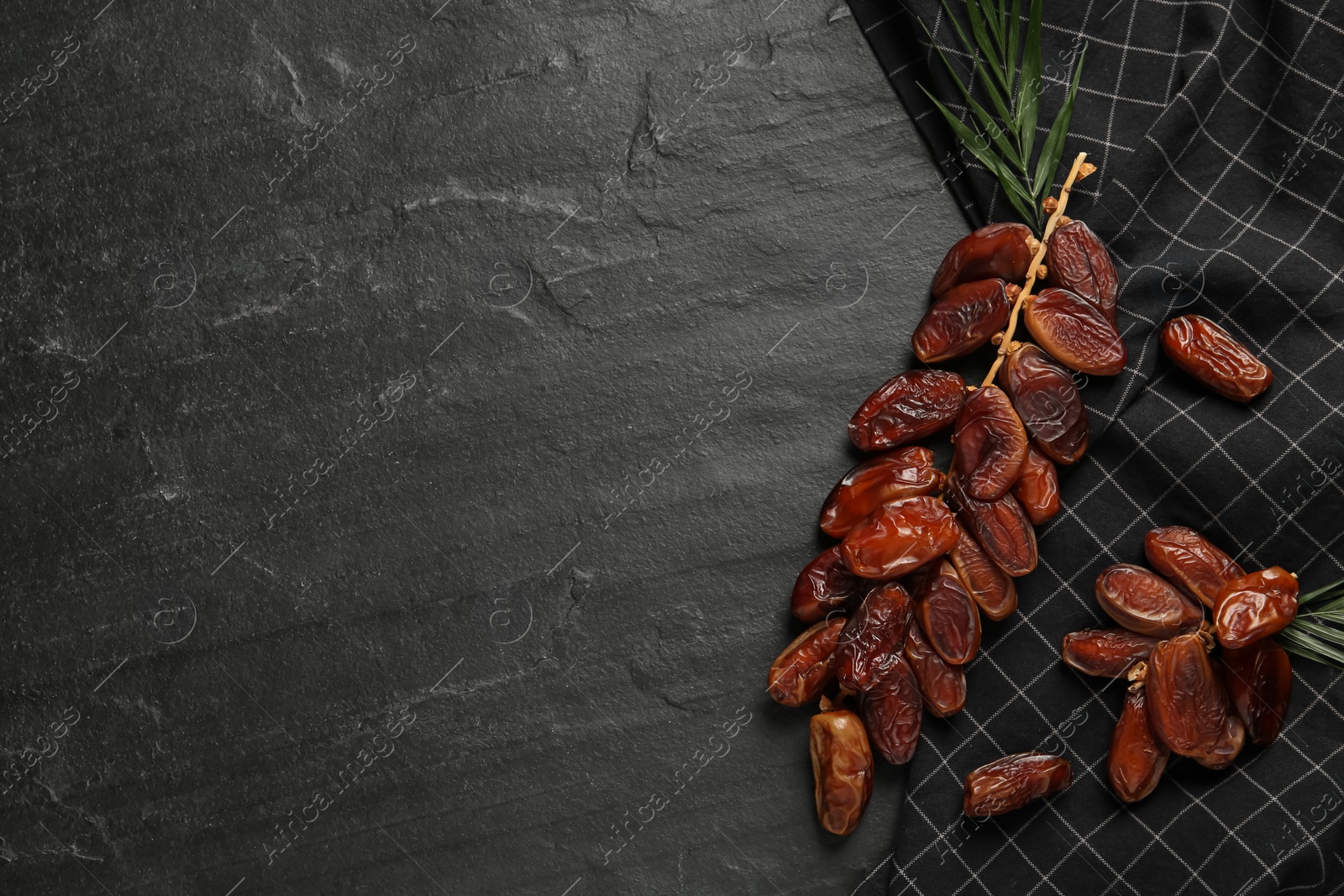 Photo of Branches with sweet dried dates and green leaf on black table, flat lay. Space for text
