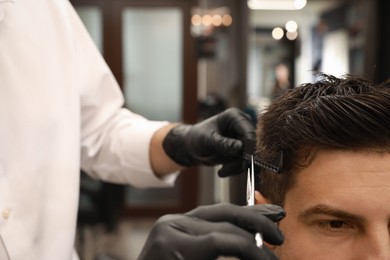 Photo of Professional hairdresser making stylish haircut in salon, closeup