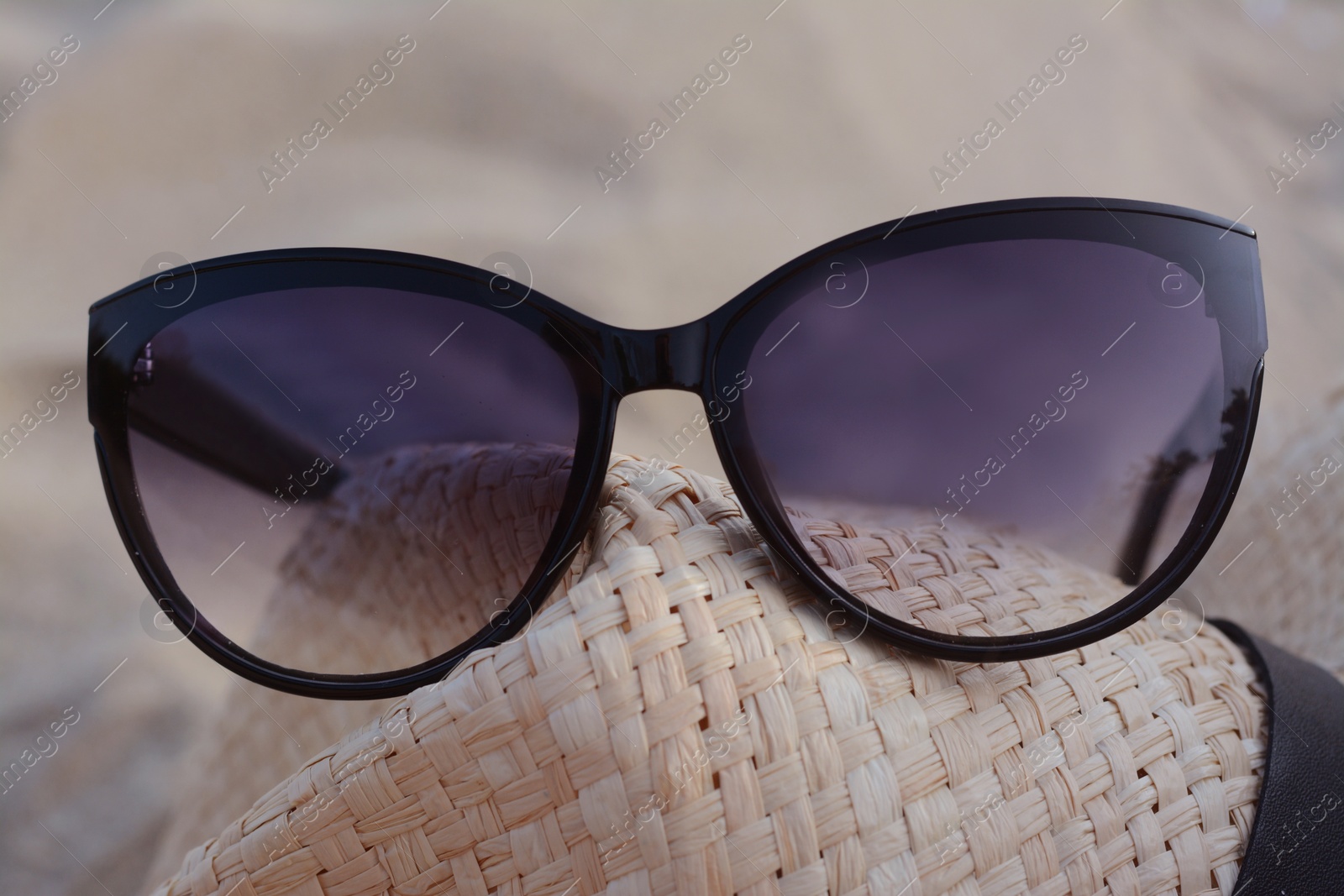 Photo of Hat with beautiful sunglasses on sandy beach, closeup