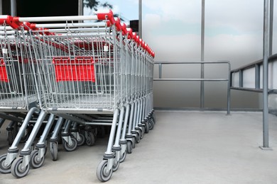 Photo of Many empty metal shopping carts near supermarket outdoors, space for text