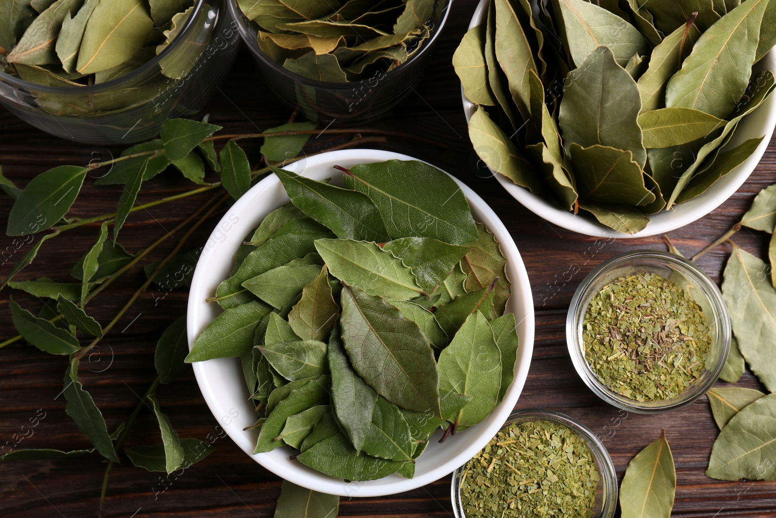 Photo of Bowls with ground, fresh and dry bay leaves on wooden table, flat lay