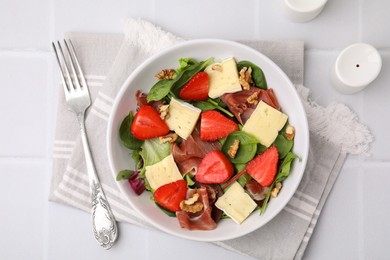 Photo of Tasty salad with brie cheese, prosciutto, strawberries and walnuts served on white tiled table, flat lay
