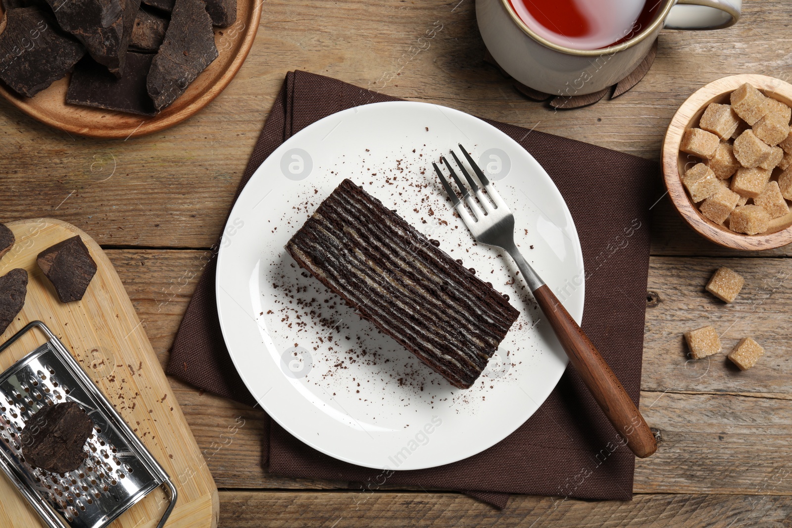 Photo of Piece of tasty chocolate cake and ingredients on wooden table, flat lay