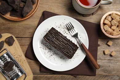 Piece of tasty chocolate cake and ingredients on wooden table, flat lay