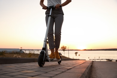 Photo of Woman riding electric kick scooter outdoors at sunset, closeup