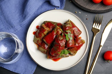 Delicious stuffed grape leaves with tomato sauce on black table, flat lay