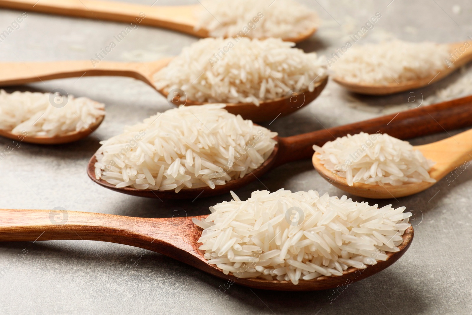 Photo of Raw basmati rice in spoons on grey table, closeup