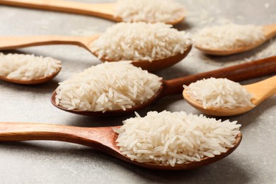 Photo of Raw basmati rice in spoons on grey table, closeup