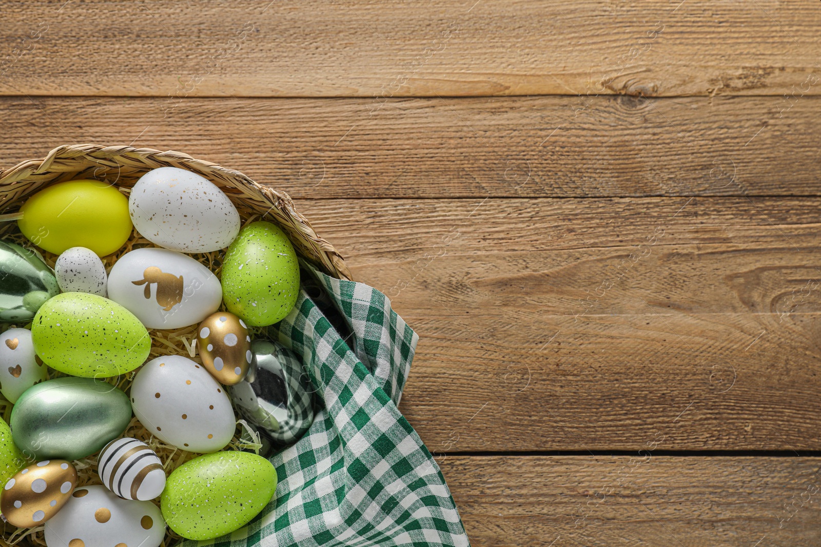 Photo of Many beautifully decorated Easter eggs in wicker basket on wooden table, top view. Space for text