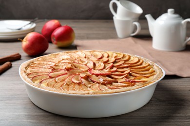 Tasty apple pie in baking dish on wooden table